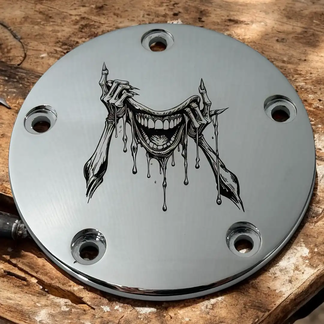 Polished motorcycle timing cover engraved with a detailed grinning figure