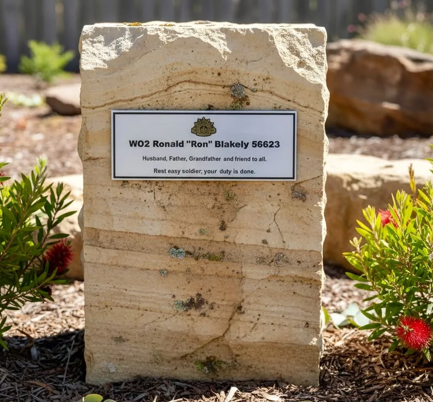 Outdoor memorial plaque mounted on a sandstone garden marker