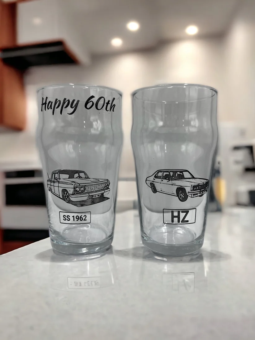 Two personalised pint glasses engraved with classic car designs and Happy 60th wording